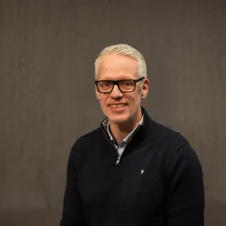 Mann med svarte briller smiler mot kamera