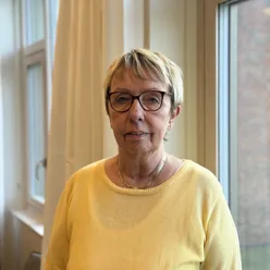 En voksen dame med kort lyst hår og briller ser i kamera