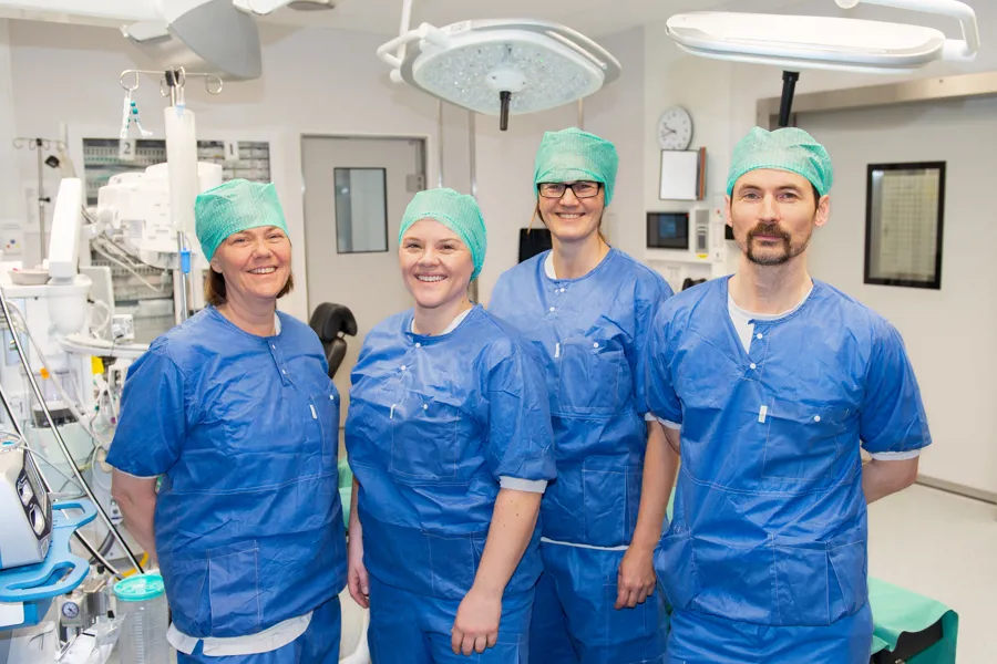 Tre damer og en mann står ikledt operasjonsklær